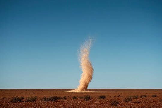 A dusty whirlwind dances across a desolate, arid landscape under a clear blue sky
