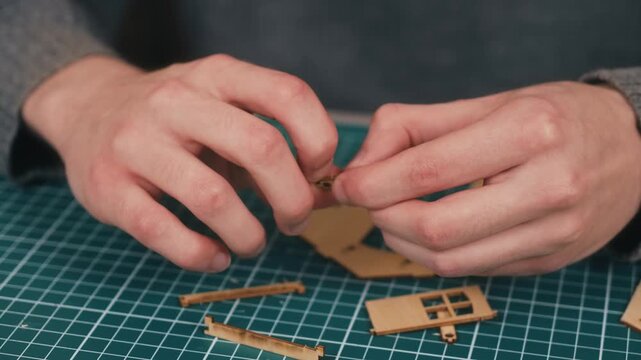 Cleaning wooden miniature house components from burrs during model assembly. DIY architecture crafting featuring plywood detail preparation and precision home construction hobby. Handcrafted housing