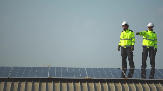 Two engineers stand talking on the darkened array at dusk, reviewing the completed installation as the city dims around the rooftop, filmed on a sustainable green energy building project in