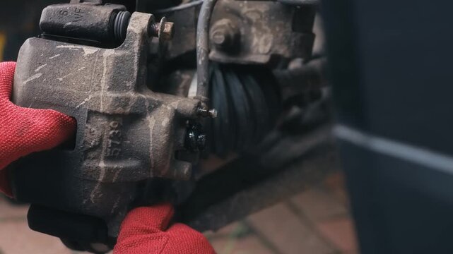 Freeing stuck caliper bracket by hand during vehicle maintenance procedure. Automotive repair concept with exposed disc assembly, closeup mechanical disassembly and manual troubleshooting. DIY car