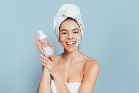 Happy woman showcasing skincare routine against soft blue background