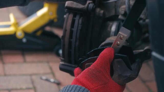 Compressing brake caliper piston with specialized repair tool during car brake maintenance. Repairing vehicle braking system with hands retracting brake cylinder for pad replacement outdoors