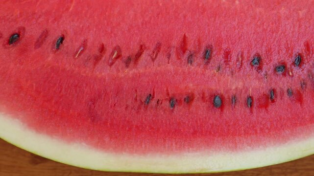 Close up slider shot moving along the slice line of a ripe red watermelon on a wooden table. Cinematic macro footage for summer beverage commercial, organic food and refreshing fruit video concept.