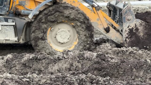 Large tractor wheels move through deep thick mud at a construction site, heavy industrial work, dirty machinery scene, construction site challenges, rugged off-road power.