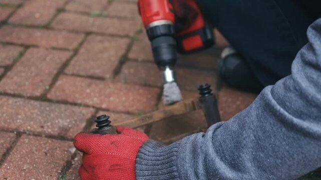 Gloved hands removing rust from brake caliper bracket with rotary wire brush. Full surface corrosion cleaning preparing brake hardware for reassembly. DIY automotive repair restoring metal caliper