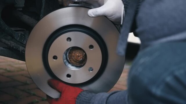 Installing new brake disc onto wheel hub during replacement process. DIY automotive repair fitting fresh rotor for restored braking performance. Vehicle maintenance preparing front brake assembly for