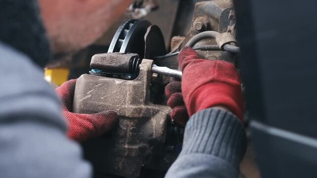 Auto mechanic installing caliper guide pins during vehicle brake repair. Close up automotive maintenance with gloved hands fastening mounting bolts on brake assembly. Car braking system reassembly and