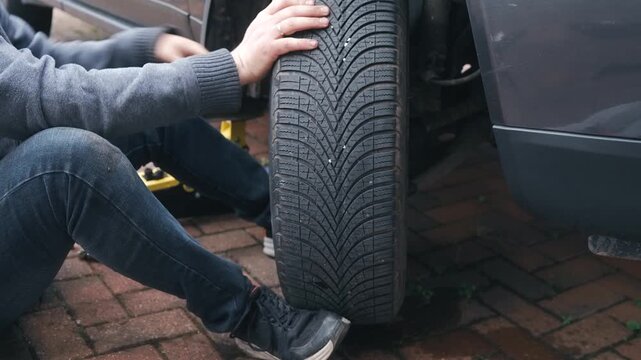 Tire mounting onto passenger car hub during automotive wheel installation. Driver aligning wheel for reassembly after brake maintenance beside lifted vehicle. Car repair process and mechanical wheel
