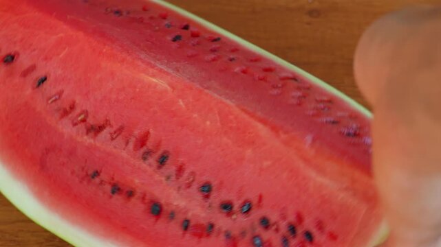 A slice of ripe red watermelon rotating on a textured wooden table surface with a static camera view. High speed fps footage for summer food commercial, organic fruit and refreshing dessert video. 