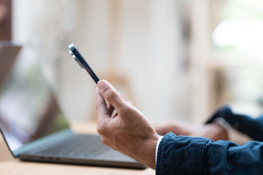 Hands of business man holding mobile phone during using laptop computer on table