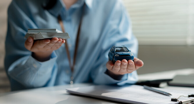 Businesswoman holding stack of cash money and car at office desk. Concept of auto loan, buying new vehicle, financial planning and car insurance investment market.