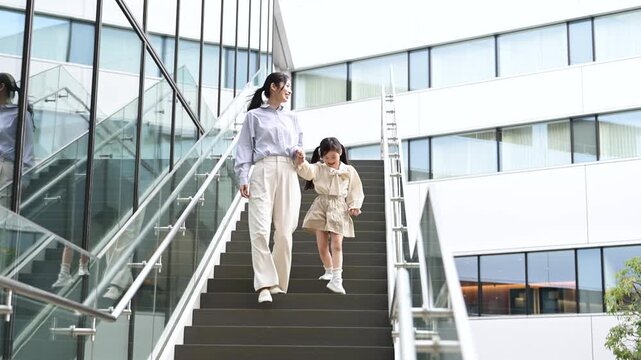 階段を降りながら笑顔で歩く30代日本人女性と6歳の女の子