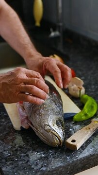 Vertical close-up of preparing fresh whole meagre fish  with sliced vegetables for homemade healthy family dinner in home kitchen, fish recipes, omega 3 diet