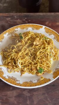 Freshly cooked Indonesian fried noodles being served onto a plate. Close-up footage of a traditional noodle dish with vegetables and chicken, showcasing authentic street food preparation and Asian cul