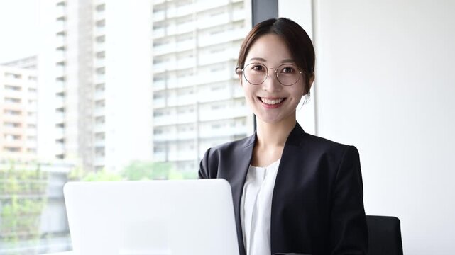 眼鏡をかけて笑顔でノートパソコンを使う20代日本人女性