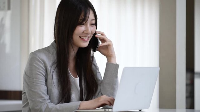 ノートパソコンを見ながら笑顔で通話をする20代日本人女性