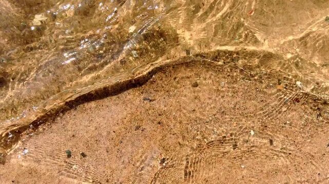Sandy lakeshore with foamy shallow waves washing over wet pebbled sand creating natural texture