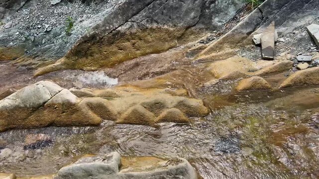 Close-up, transparent water murmurs around smooth yellowish stones with bizarre depressions against the background of gray rocks. Concept: Mountain stream, spring water. High quality 4k footage