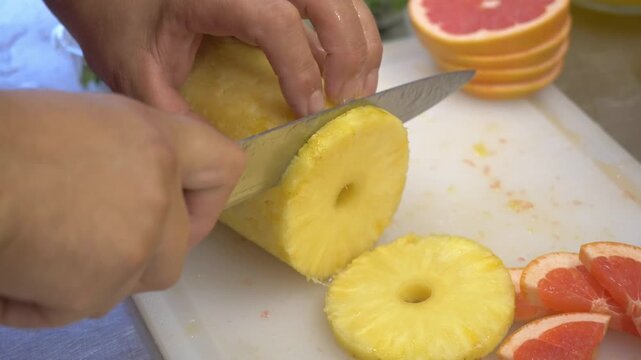 Fresh pineapple is sliced into pieces for cocktails and refreshing beverages prepared during a festive restaurant catering service.