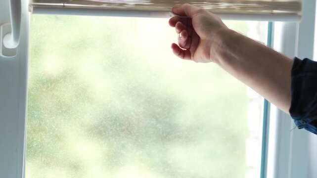 Close up of a hand pulling down white pleated window blinds to block light