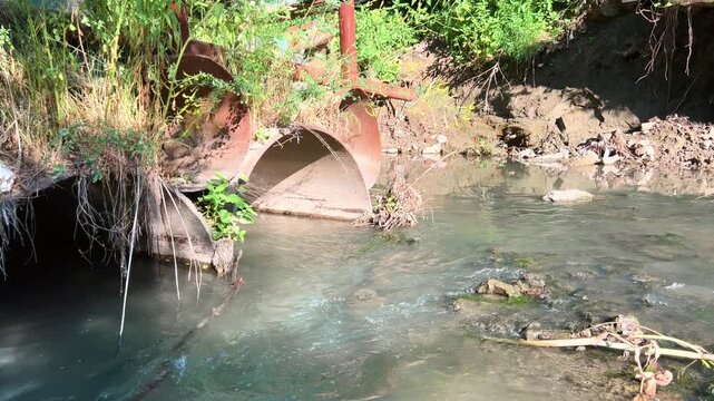 Old drainage pipe discharging water into muddy polluted river stream