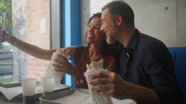 Latina woman and Caucasian man taking selfie while eating tortillas at fast food restaurant
