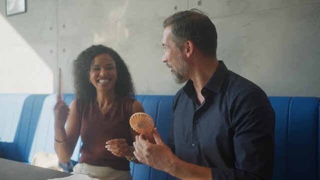 Diverse couple cooling down with fan during extreme El Ni&ntilde;o heat wave at home