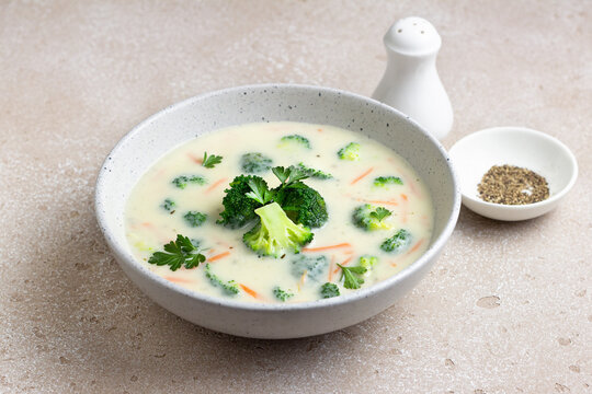 Homemade creamy broccoli soup with potatoes carrots and parsley in ceramic bowl on light textured background
