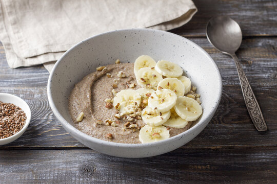 Healthy flaxseed porridge topped with banana slices, chopped nuts and seeds in a ceramic bowl. Nutritious breakfast with natural ingredients, copy space