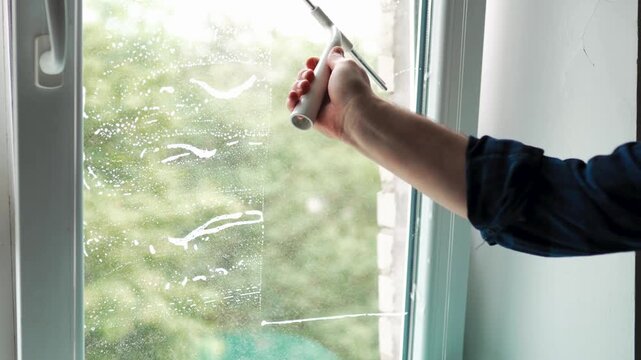 Close up of a man hand using a window squeegee scraper to remove water from glass