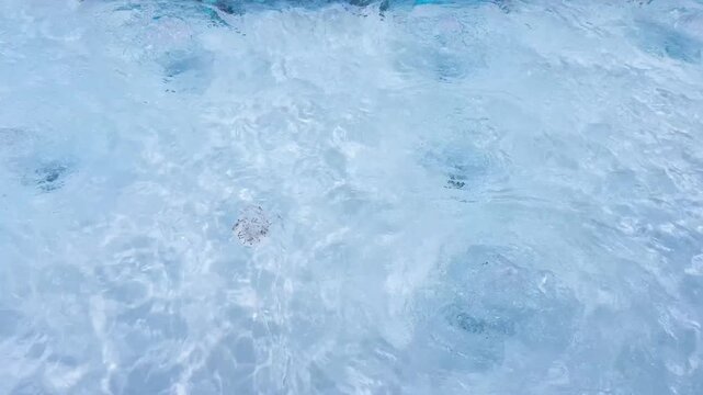 The bubbling water in the pool's jacuzzi is actively bubbling on the light blue surface. Jacuzzi hydromassage concept, relaxation and relaxation, water treatments, summer bath. High quality 4k footage