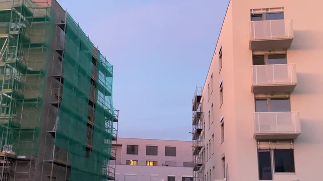 Modern residential building under construction covered with green protective safety netting on a warm summer evening. Construction site with unfinished facade. Urban development 