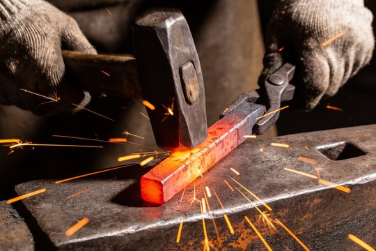 A blacksmith strikes a glowing red-hot steel bar on an anvil, creating a shower of bright sparks.