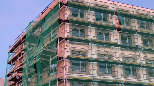 Modern residential building under construction covered with green protective safety netting on a warm summer evening. Construction site with unfinished facade. Urban development 