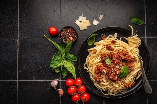 Pasta spaghetti bolognese with minced beef sauce, tomatoes, parmesan cheese and fresh basil in a plate on black tile background. Italian food, top view