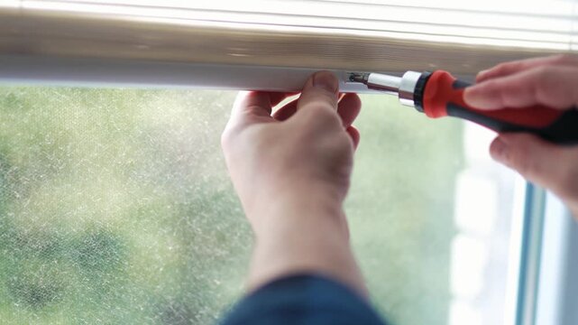 Close up of a handyman hand adjusting a white window sunshade with a tool