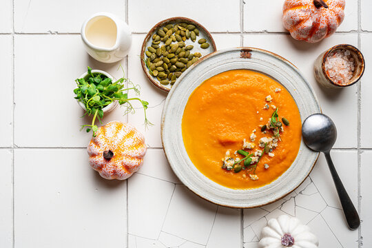 Pumpkin soup with gorgonzola cheese in white plate on white tile background, top view
