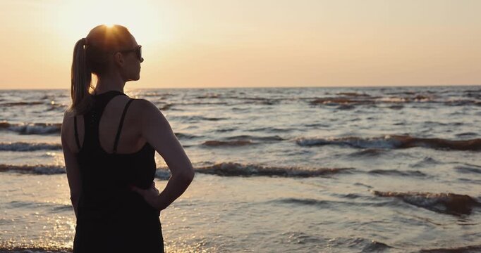 fitness woman in black sportsware enjoying sunset on the beach after workout