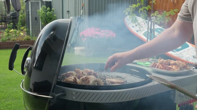 A man places bread slices on a hot outdoor charcoal grill grate during a backyard barbecue cookout. Fresh slices toast next to juicy chicken skewers for a delicious summer family meal outdoors.