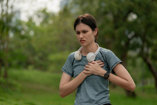 Young woman holding chest in pain during outdoor workout, wearing headphones and smartwatch, health emergency, heart problem, fitness risk and active lifestyle, chest, pain, heart, health, emergency.
