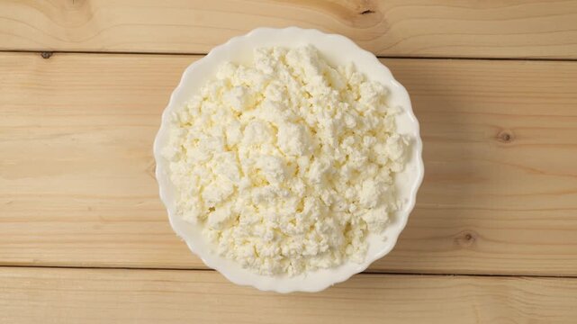Rotating white bowl of cottage cheese on a wooden table