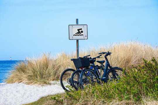In the dunes on a Baltic Sea beach, three bicycles are leaning against a "Bathing Beach" sign. 