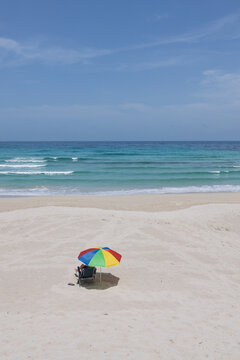 Person relaxing under colorful umbrella on empty beach