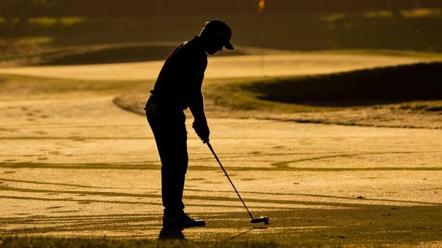 Addressing ball, golfer with cap and shoes tensing grip with putter on sunlit-green, preparing putt