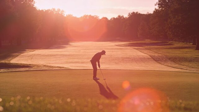 Addressing ball, male golfer wearing cap and polo aligning, stroking putter to sink ball on green