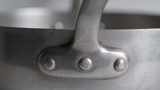 Shifting camera showing riveted saucepan handle with three rivets in studio, revealing maker's mark