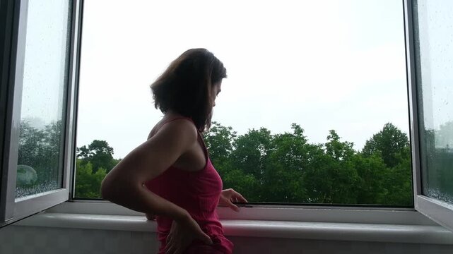 Woman looking out of window at trees on a rainy day