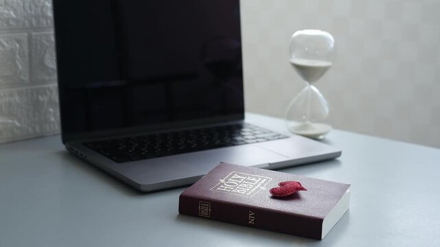 Modern workspace with a laptop, hourglass, and a holy book Bible on the table