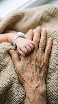 Cute newborn hand placed on top of an aged, wrinkled senior citizen's hand wearing a wedding ring.