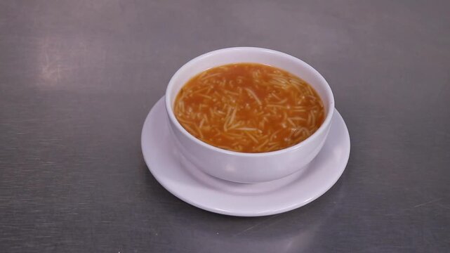 Sirviendo sopa de fideos en plato hondo blanco. Sopa de fideos reci&eacute;n servida en restaurante. Cuchar&oacute;n de metal sirviendo sopa tradicional. Comida casera mexicana en proceso de servicio.